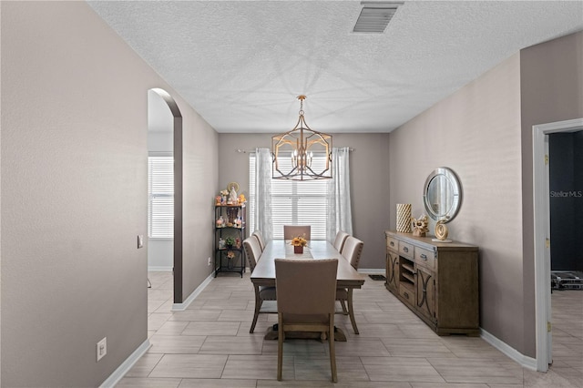 dining room featuring arched walkways, visible vents, an inviting chandelier, a textured ceiling, and baseboards