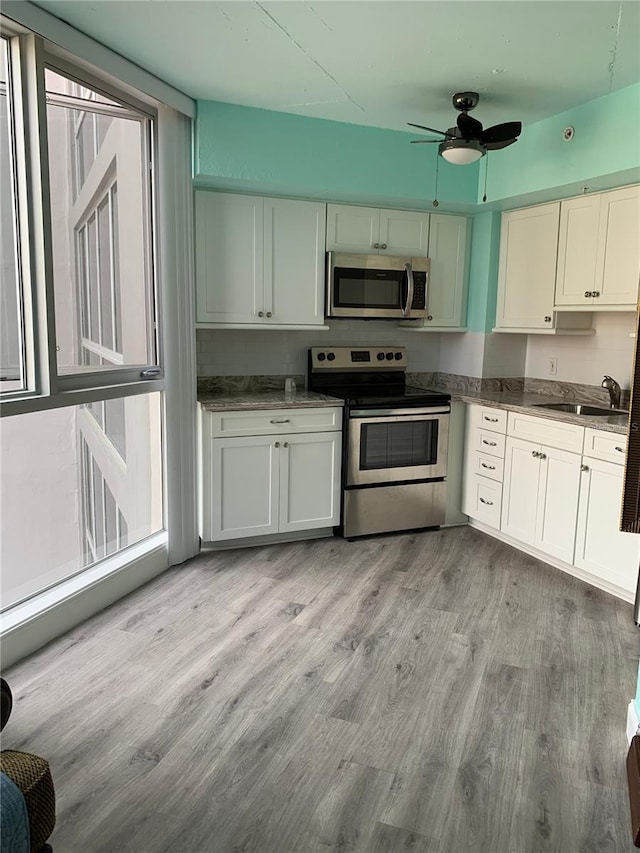 kitchen featuring stainless steel appliances, light wood-style floors, a ceiling fan, white cabinets, and a sink