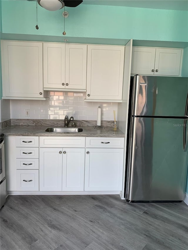 kitchen with wood finished floors, a sink, freestanding refrigerator, and white cabinets