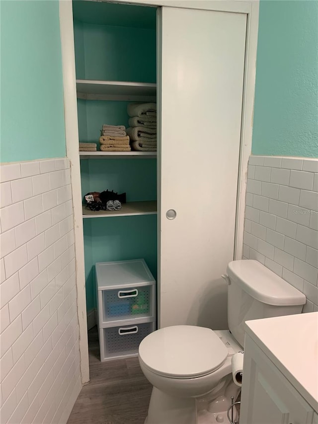 bathroom featuring a wainscoted wall, tile walls, toilet, vanity, and wood finished floors