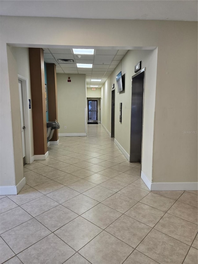 corridor with baseboards, visible vents, elevator, a paneled ceiling, and light tile patterned flooring