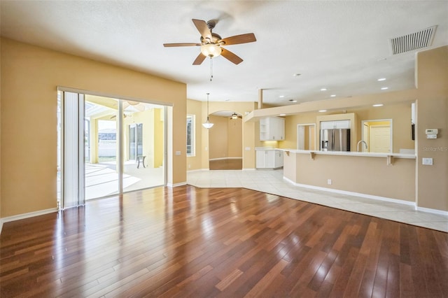 unfurnished living room with light wood-style floors, baseboards, visible vents, and a ceiling fan