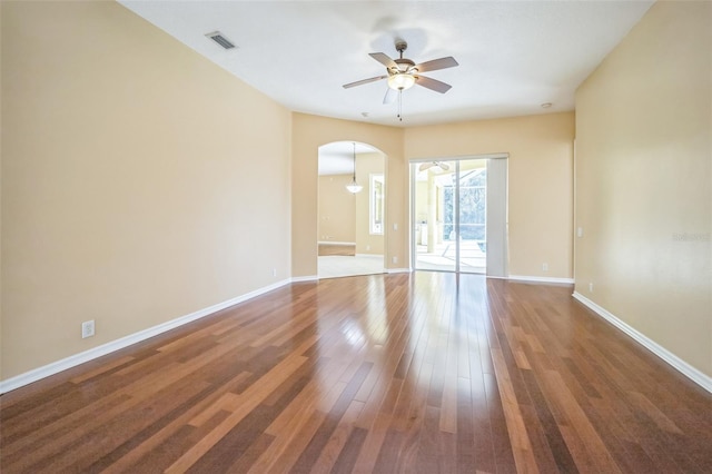 unfurnished room featuring arched walkways, wood finished floors, visible vents, and baseboards