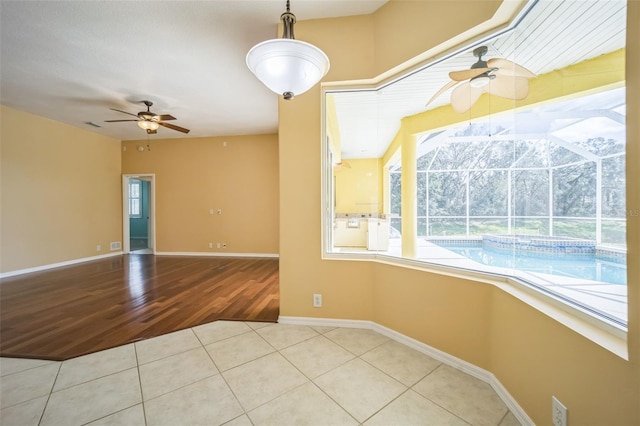 empty room with a ceiling fan, a sunroom, baseboards, and tile patterned floors