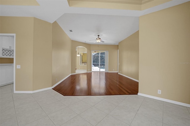 spare room featuring light tile patterned floors, baseboards, visible vents, arched walkways, and a ceiling fan