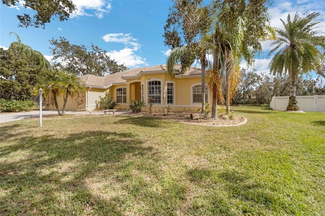 mediterranean / spanish-style house featuring a tile roof, stucco siding, concrete driveway, a front yard, and fence