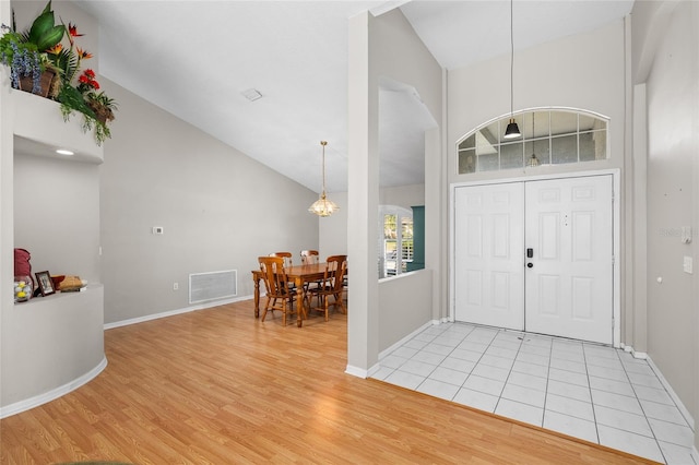 foyer entrance with visible vents, a chandelier, baseboards, light wood-style flooring, and high vaulted ceiling