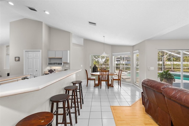 kitchen featuring lofted ceiling, light tile patterned flooring, visible vents, a sunroom, and a kitchen breakfast bar