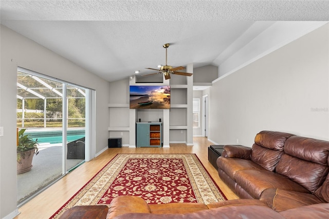 living room with lofted ceiling, a sunroom, wood finished floors, a textured ceiling, and built in shelves