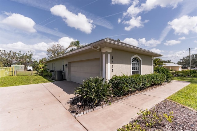 view of home's exterior featuring stucco siding, a lawn, central AC unit, fence, and driveway