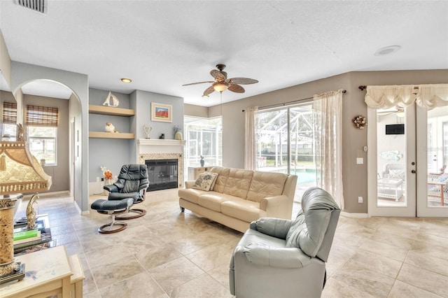 living area featuring baseboards, visible vents, a ceiling fan, a tile fireplace, and french doors