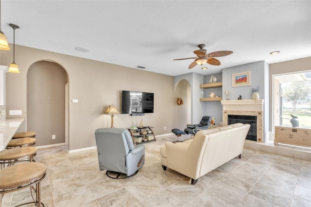 living area featuring arched walkways, a fireplace, a ceiling fan, visible vents, and baseboards