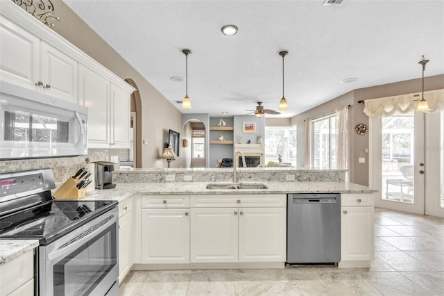 kitchen featuring white cabinets, appliances with stainless steel finishes, a peninsula, light stone countertops, and a sink