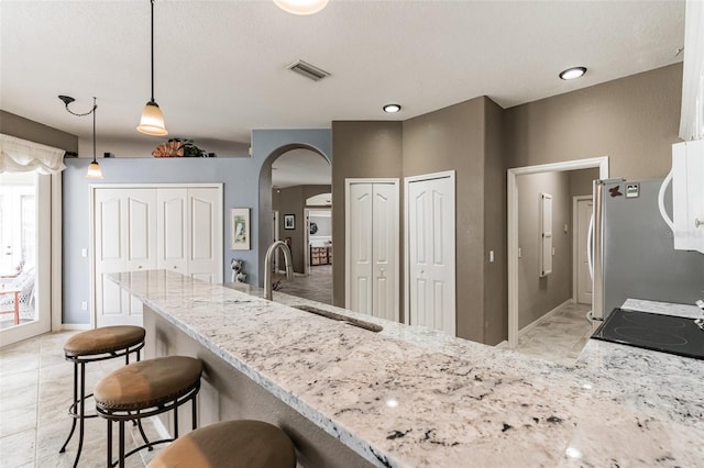 kitchen featuring visible vents, arched walkways, freestanding refrigerator, light stone countertops, and a sink