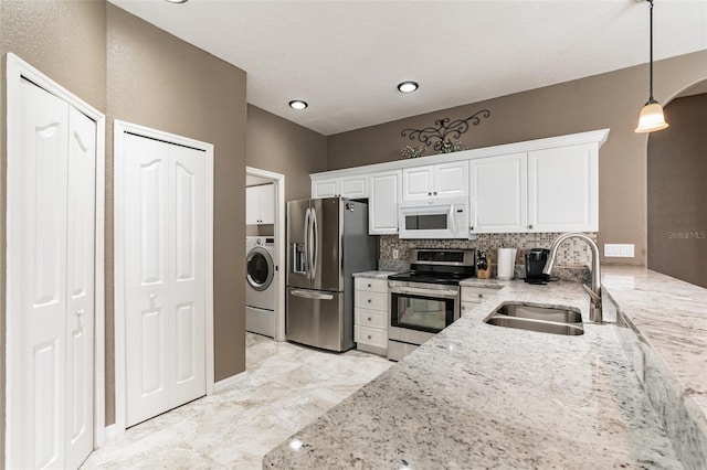 kitchen with stainless steel appliances, white cabinetry, a sink, light stone countertops, and washer / dryer