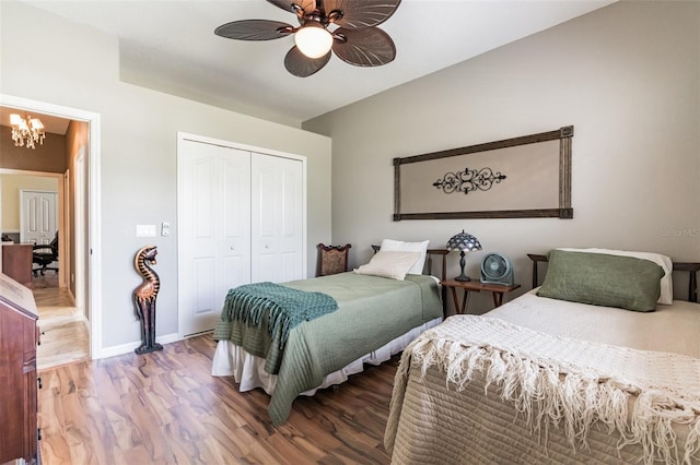 bedroom featuring ceiling fan with notable chandelier, a closet, baseboards, and wood finished floors