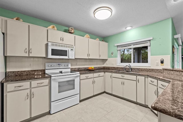 kitchen with white appliances, dark stone countertops, a sink, and decorative backsplash