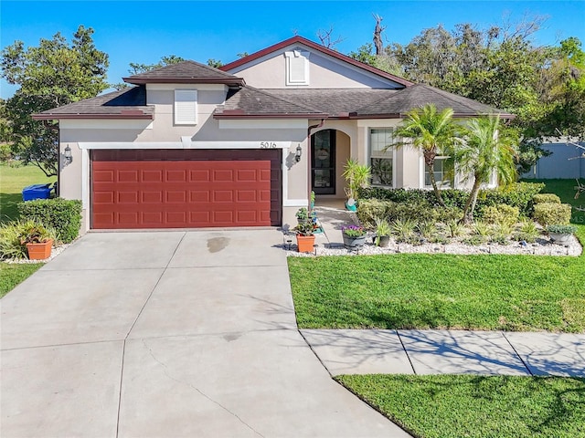 view of front of property featuring a front yard, an attached garage, driveway, and stucco siding