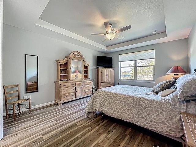 bedroom featuring ceiling fan, a raised ceiling, baseboards, and wood finished floors