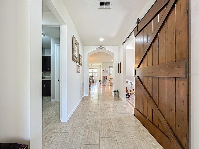 hall with wood finish floors, visible vents, arched walkways, and baseboards