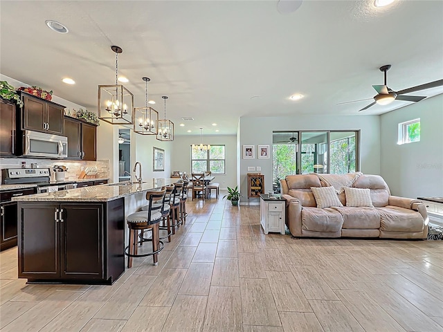 kitchen featuring dark brown cabinetry, open floor plan, decorative backsplash, ceiling fan with notable chandelier, and stainless steel appliances