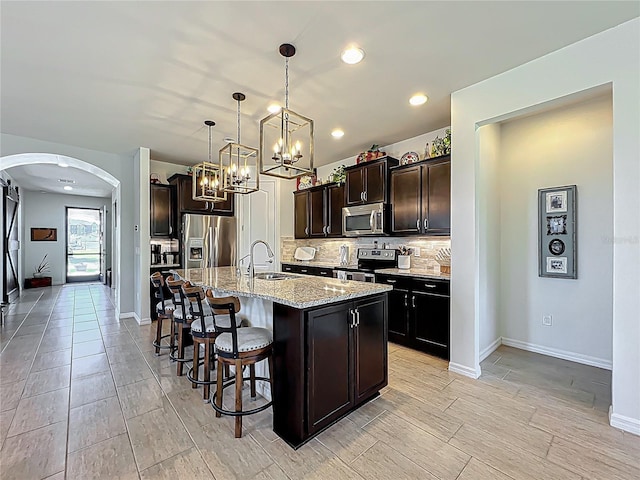 kitchen featuring a breakfast bar, decorative backsplash, arched walkways, stainless steel appliances, and a sink