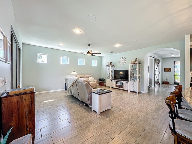 living area with visible vents, a barn door, arched walkways, baseboards, and ceiling fan