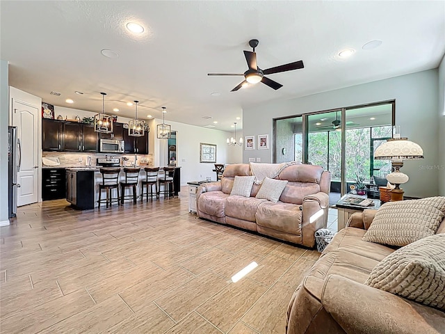 living area featuring recessed lighting, light wood-style floors, and ceiling fan with notable chandelier