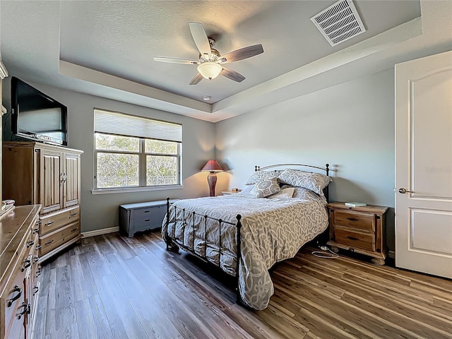 bedroom featuring a ceiling fan, a raised ceiling, wood finished floors, and visible vents