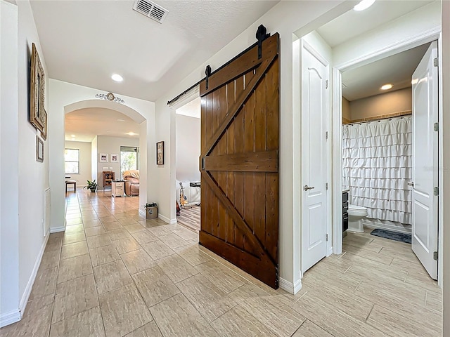 corridor with visible vents, recessed lighting, a barn door, arched walkways, and baseboards