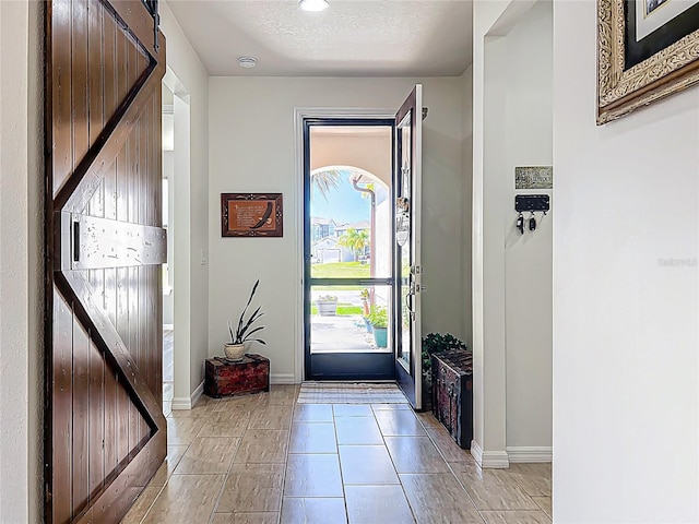 foyer entrance featuring light tile patterned floors, a barn door, baseboards, and a textured ceiling