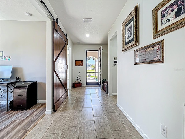 interior space with a barn door, visible vents, baseboards, and a textured ceiling