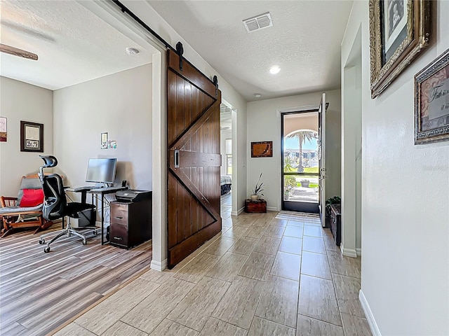 entrance foyer with a barn door, visible vents, light wood finished floors, and a textured ceiling