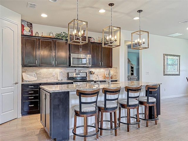 kitchen with light stone counters, visible vents, appliances with stainless steel finishes, a kitchen bar, and backsplash