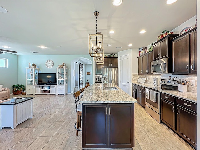 kitchen with a center island with sink, a sink, open floor plan, arched walkways, and appliances with stainless steel finishes