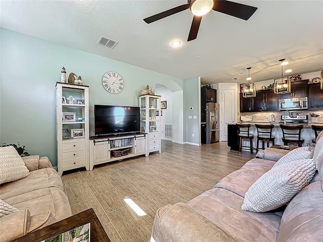 living room featuring arched walkways, visible vents, light wood finished floors, and ceiling fan