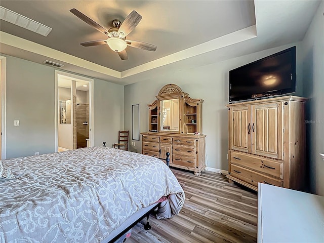 bedroom featuring a tray ceiling, wood finished floors, and visible vents