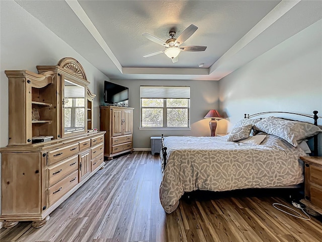 bedroom featuring baseboards, a raised ceiling, ceiling fan, and dark wood-style flooring