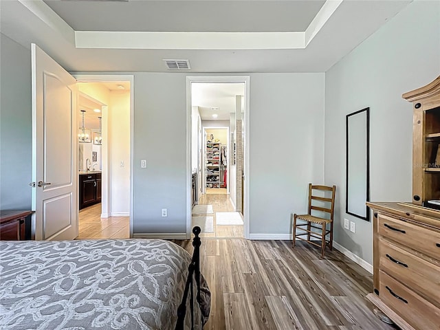 bedroom featuring visible vents, baseboards, a raised ceiling, and light wood-style floors