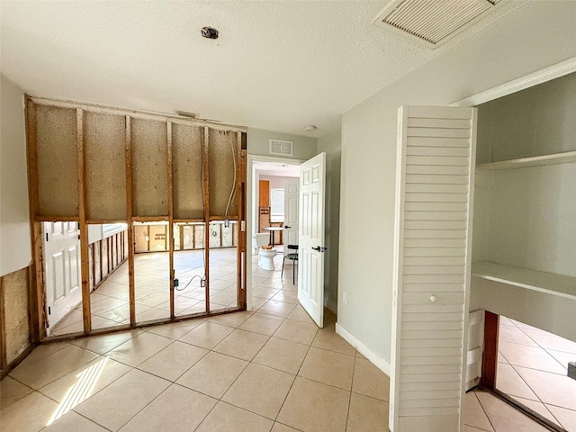 unfurnished bedroom with a closet, visible vents, a textured ceiling, and light tile patterned floors