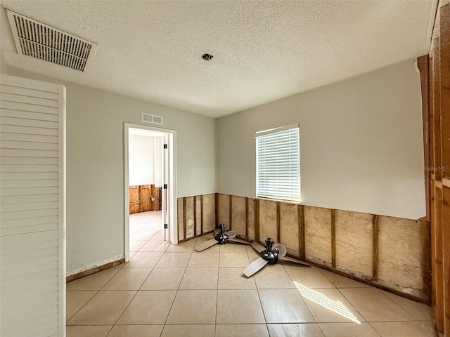 empty room with a wainscoted wall, light tile patterned floors, a textured ceiling, and visible vents