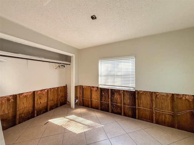 unfurnished room featuring a wainscoted wall, a textured ceiling, and tile patterned floors