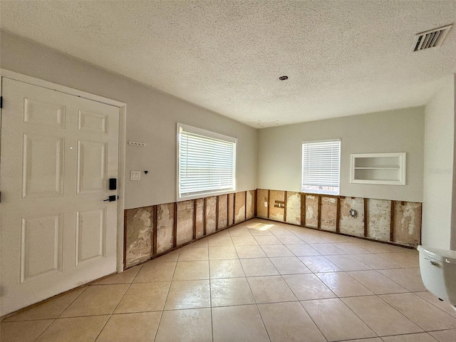 unfurnished room featuring a wainscoted wall, visible vents, a textured ceiling, and light tile patterned floors