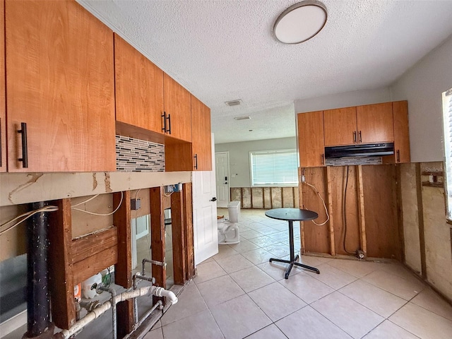 kitchen featuring light tile patterned floors, under cabinet range hood, visible vents, brown cabinets, and tasteful backsplash