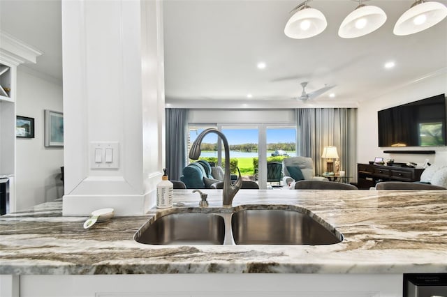 kitchen with crown molding, a ceiling fan, open floor plan, a sink, and light stone countertops