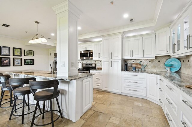 kitchen with stone tile floors, visible vents, a kitchen breakfast bar, ornamental molding, and appliances with stainless steel finishes