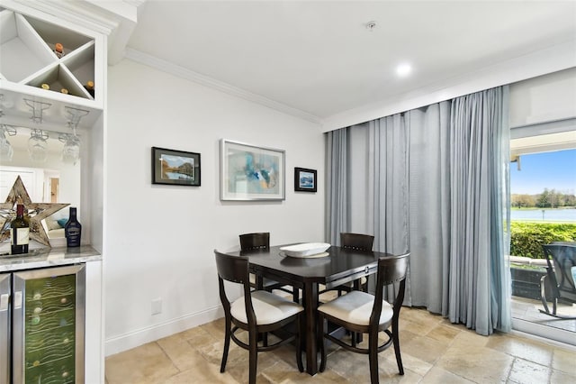 dining area featuring a dry bar, baseboards, wine cooler, ornamental molding, and stone tile flooring