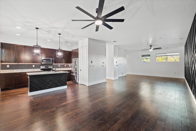 kitchen with stainless steel appliances, dark brown cabinets, open floor plan, and decorative backsplash