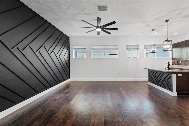 unfurnished living room with ceiling fan with notable chandelier, dark wood-style floors, visible vents, and baseboards