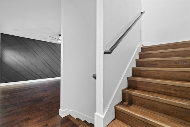 stairway with baseboards, wood finished floors, a ceiling fan, and wood walls